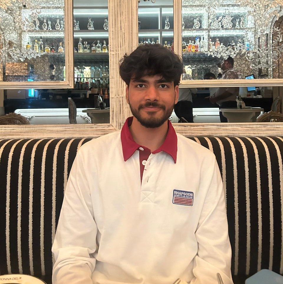 Pratham Garg in a white rugby polo, smiling at a cafe